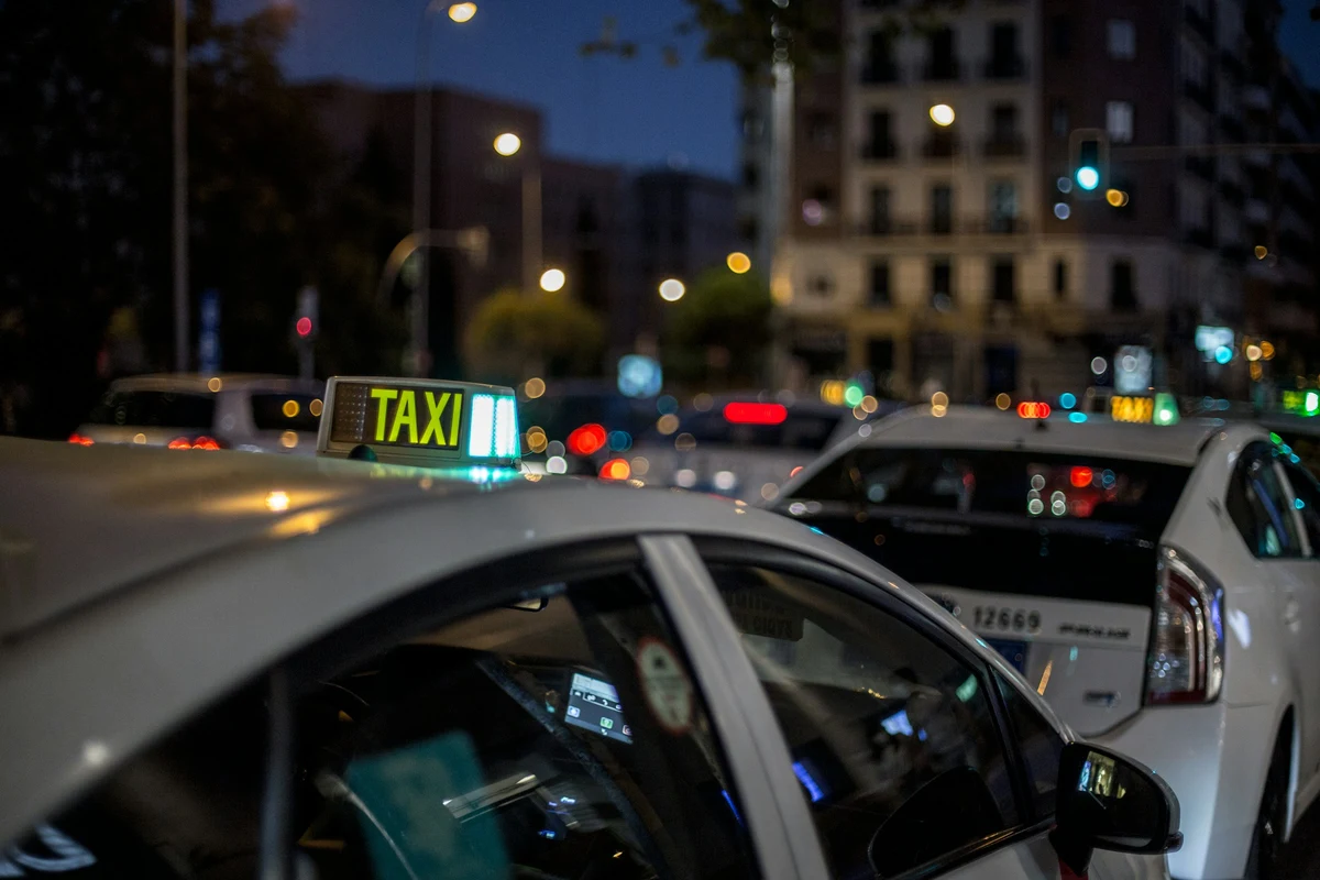 Taxis blancos en fila de noche, con el letrero TAXI iluminado en verde sobre el techo